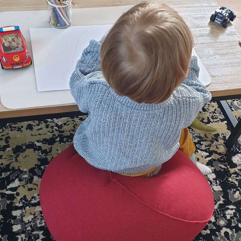 Kind sitzt vor einem Tisch mit Papier, Stiften und Spiesache.